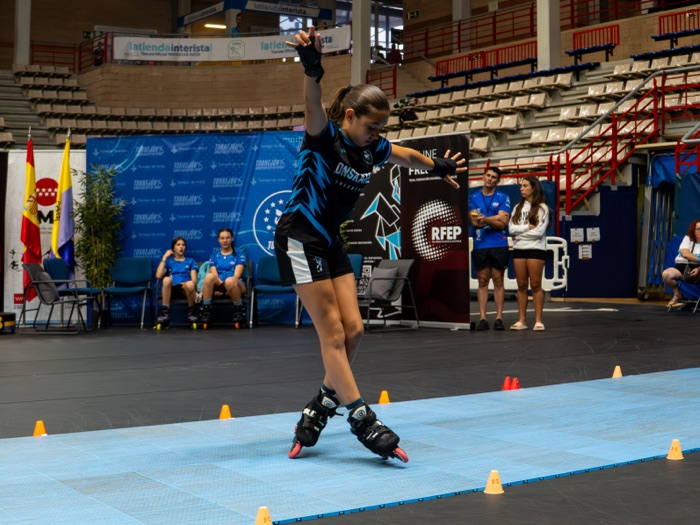 Patinadora de Onskates en equilibrio controlado a una pierna tras un derrape, con banner del club y de la RFEP al fondo