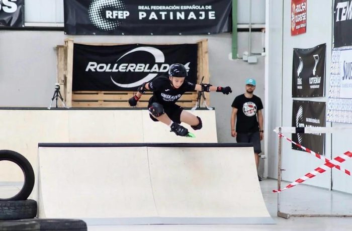 Patinador saltando un obstáculo de rampa en una prueba de Skate Cross, con casco y protecciones completas
